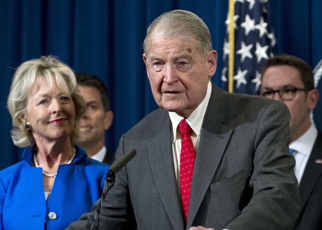 FILE - Former FBI director and CIA director William Webster, right, accompanied by his wife Lynda Webster, who were targeted by a man who peddled a lottery scam over phone calls and emails, speaks during a news conference to address elder financial exploitation and law enforcement actions, at the Department of Justice in Washington, March 7, 2019. (AP Photo/Jose Luis Magana, File)