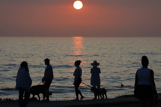 People gather along the La Jolla coastline as the sun sets on the horizon of the Pacific Ocean while smoke from Southern California wildfires fills the air on August 5, 2025 in San Diego, California.