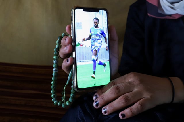 Doaa, the widow of late soccer player Suleiman Al-Obeid, known as the "Palestinian Pele," who was killed by an Israeli strike targeting people waiting for humanitarian aid, according to the Palestine Football Association, shows a picture of him on a mobile phone inside their tent in Gaza City August 9, 2025. REUTERS/Ebrahim Hajjaj