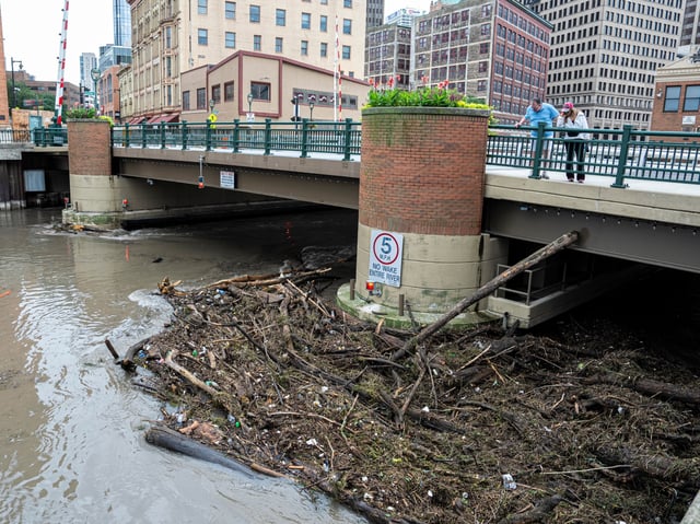 MILWAUKEE, WISCONSIN - AUGUST 10: People watch as debris piles up on a bridge piling on the Milwaukee River after heavy rain in the area on August 10, 2025 in Milwaukee, Wisconsin. Heavy downpours brought as much as 13 inches of rain to parts of southeast Wisconsin overnight, resulting in widespread flooding across the region. (Photo by Andy Manis/Getty Images)