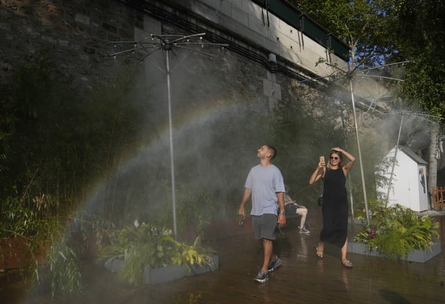People cool off under showers at Paris Plage along the Seine river in Paris, Sunday, Aug. 10, 2025. (AP Photo/Michel Euler)