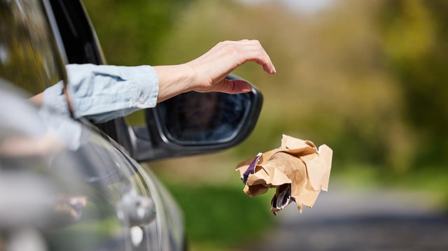 Eine Person wirft Müll aus einem fahrenden Auto.