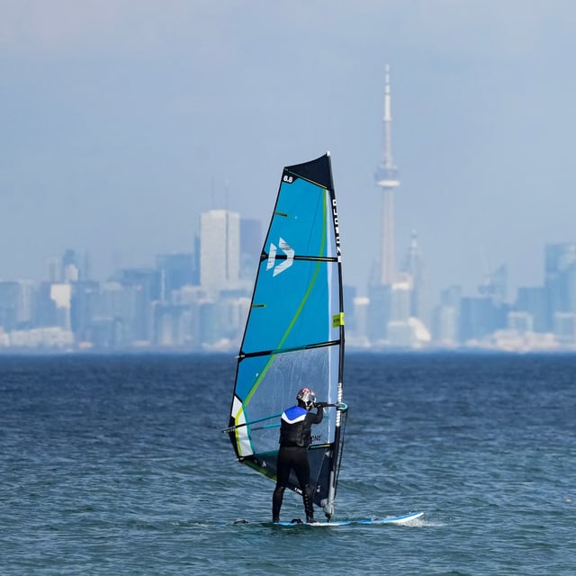 A windsurfer cuts through the waves along Lake Ontario overlooking the City of Toronto skyline on a warm winter day in Mississauga, Ont., Friday, Feb. 9, 2024. THE CANADIAN PRESS/Nathan Denette