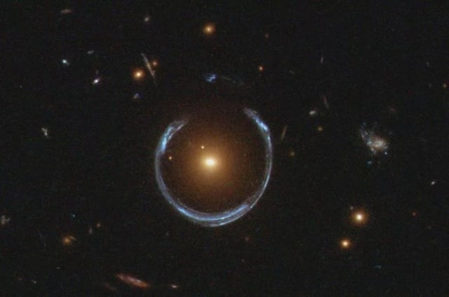 The Cosmic Horseshoe gravitational lens. The newly discovered ultramassive blackhole lies at the centre of the orange galaxy. Far behind it is a blue galaxy that is being warped into the horseshoe shaped ring by distortions in spacetime created by the immense mass of the foreground orange galaxy. Credit: NASA/ESA