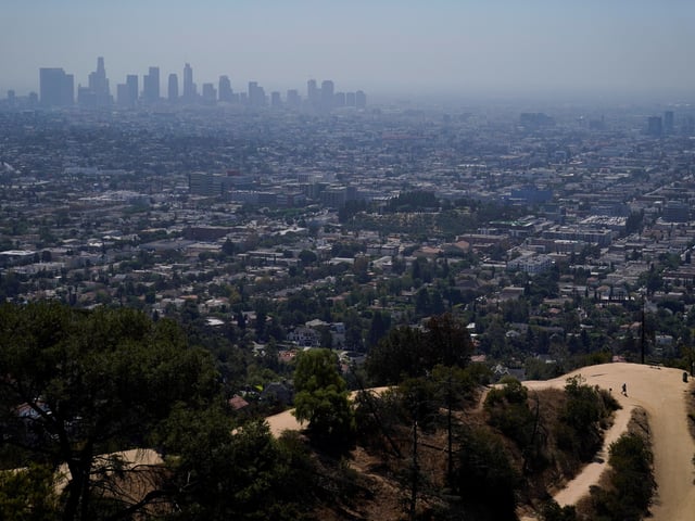 A hiker walks along a trail at Griffith Park as the hazy skyline of downtown Los Angeles is shown in the distance, Tuesday, Sept. 6, 2022,  in Los Angeles. Authorities say California is facing its highest chance of blackouts this week as a brutal heat wave continues to blanket the state with triple-digit heat. (AP Photo/Jae C. Hong)