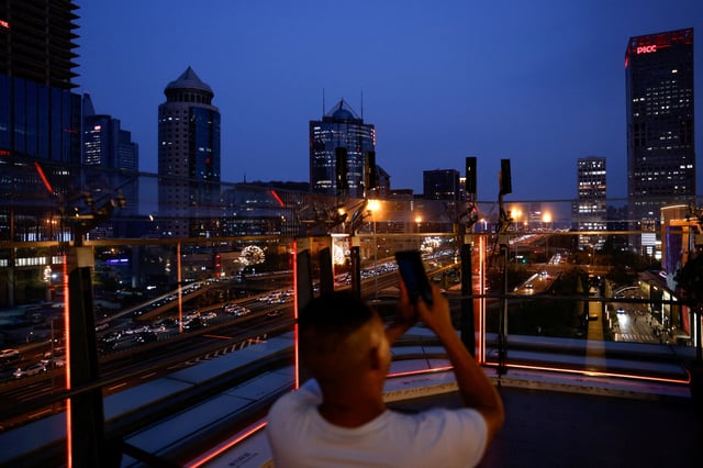 A person takes pictures on a terrace of a shopping mall overlooking the central business district (CBD), in Beijing, China August 11, 2025. REUTERS/Tingshu Wang