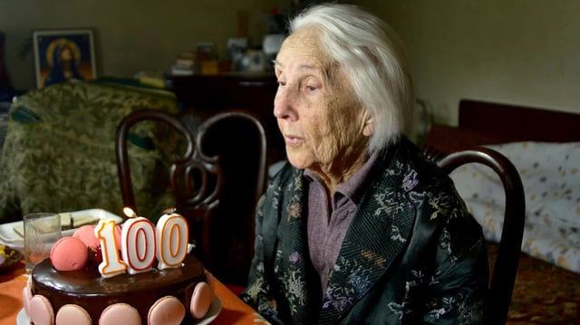 A centenarian blows out her 100th birthday candles. (Photo by Dan Negureanu on Shutterstock)