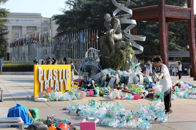 Benjamin Von Wong, a la derecha, un artista y activista canadiense, amontona pilas de desechos plásticos sobre una gran escultura que diseñó frente a la oficina de las Naciones Unidas en Ginebra, Suiza, el lunes 11 de agosto de 2025. (Foto AP/ Jennifer McDermott)
