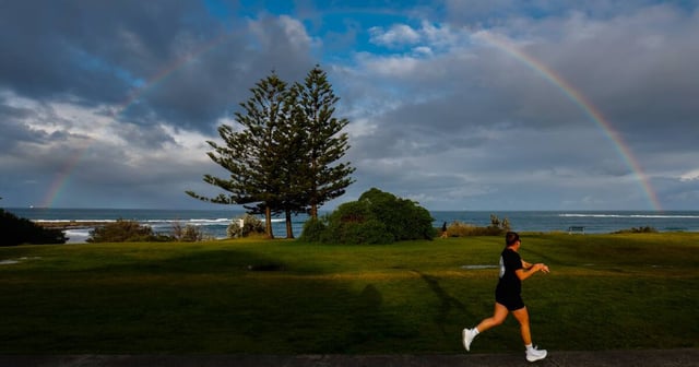 A person running under grey skies and a rainbow in Bulli on Sunday, August 10. Picture by Anna Warr