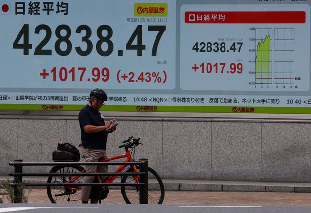 A man with a bicycle stands in front of a stock quotation board showing the Nikkei share average outside a brokerage in Tokyo, Japan, August 12, 2025. REUTERS/Kim Kyung-Hoon