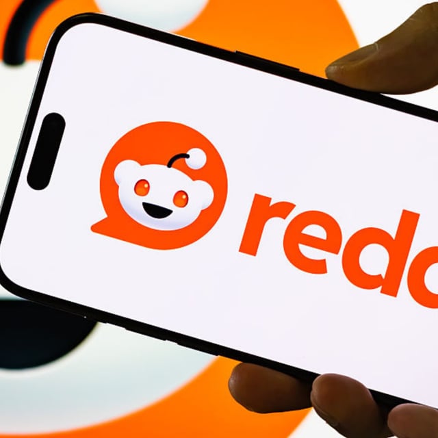 A person holds a smartphone displaying the Reddit logo.