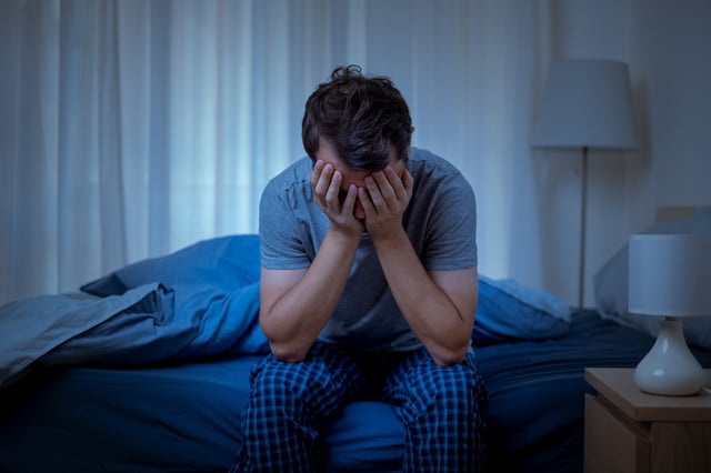 Man sitting on the edge of his bed with his hand&#39;s in his hands in the middle of the night.