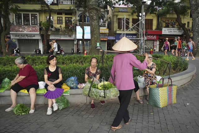 A vendor sells vegetables to people out for morning exercises in a park in Hanoi, Vietnam, Aug. 12, 2025. (AP Photo/Huy Han)