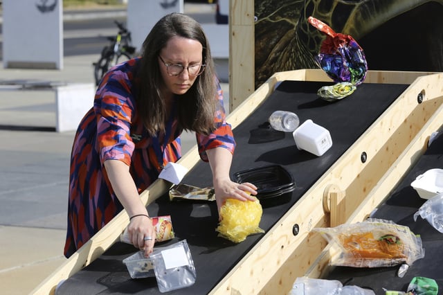 Hanna Eberhard, with the World Wildlife Fund, arranges plastic waste on a conveyor belt display in front of the United Nations office in Geneva, Switzerland, Wednesday, Aug. 13, 2025. (AP Photo/ Jennifer McDermott)