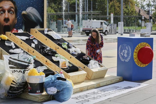 Hanna Eberhard, with the World Wildlife Fund, arranges plastic waste on a conveyor belt display in front of the United Nations office in Geneva, Switzerland, Wednesday, Aug. 13, 2025. (AP Photo/ Jennifer McDermott)