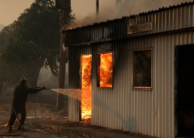 A firefighter works to extinguish a fire from a building during a wildfire, in Sichaina near Patras, Greece, August 13, 2025. REUTERS/Louiza Vradi