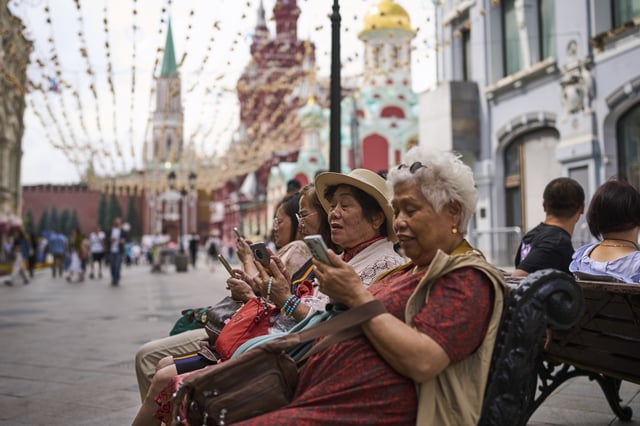 FILE - People look at their phones near the Kremlin in Moscow, July 16, 2025. (AP Photo/Alexander Zemlianichenko, File)
