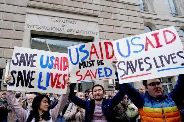People hold placards, as the USAID building sits closed to employees after a memo was issued advising agency personnel to work remotely, in Washington, D.C., U.S., February 3, 2025.
