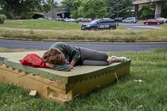 Stephanie W., 28, who is homeless, rests on a foam mattress as a United States Park Police vehicle drives past, Wednesday, Aug. 13, 2025, in northwest Washington near the Kennedy Center. (AP Photo/Jacquelyn Martin)