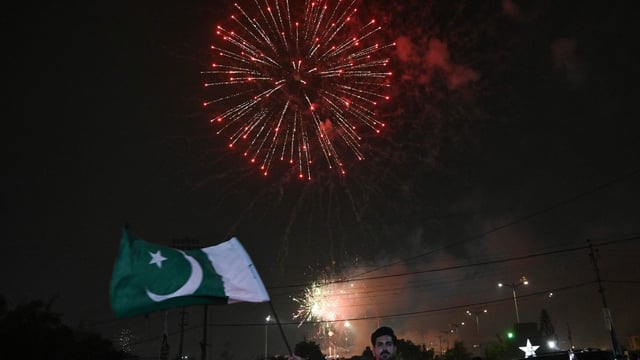 A man waves a flag of Pakistan as people watch a firework displayed in front of a stadium in Karachi on Independence Day.