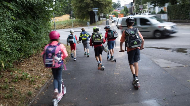 Kinder sind zu Fuß und auf Rollern auf dem Weg zur Schule.