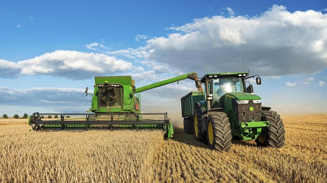 Mähdrescher erntet Weizen und entlädt Getreide auf Traktor mit Anhänger.
