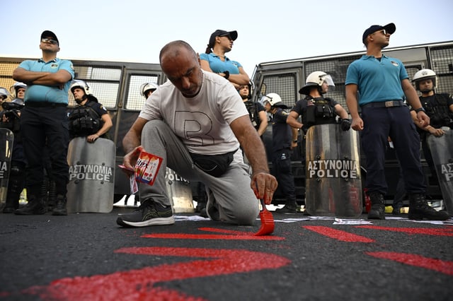 A protester paints a slogan on the ground, in front of police forces, during a rally to protest the arrival of a cruise ship with Israelis, in Piraeus port, Greece, Thursday, Aug. 14, 2025. (AP Photo/Michael Varaklas)