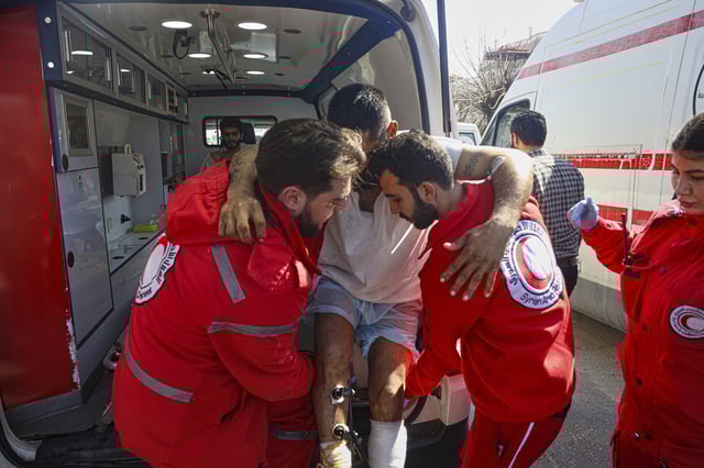 FILE - Red Crescent workers carry a wounded man outside the Russian air base in Hmeimim, near Latakia in Syria's coastal region on March 11, 2025, as they evacuate wounded members of the Alawite sect who have sought refuge there following recent violence and revenge killings. (AP Photo/Omar Albam, File)