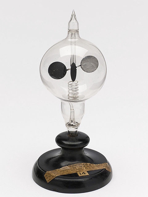 Image of a wooden stand holding a sealed glass bulb with a spinning set of vanes, each of which has a lit and dark side.