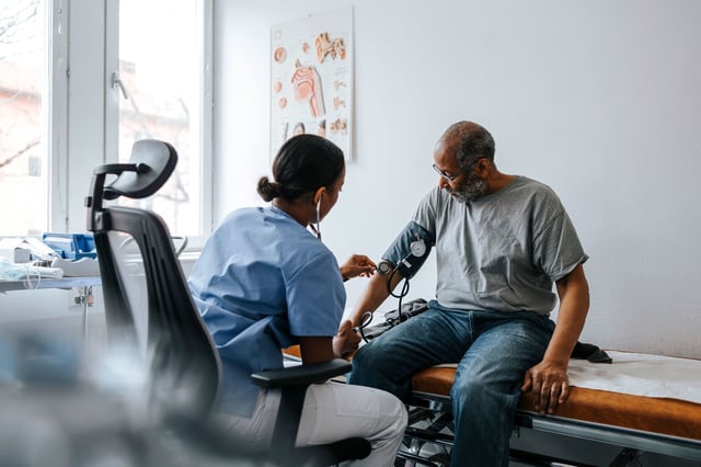 Female doctor checking senior patient's blood pressure sitting on bed in examination room at hospital - stock photo