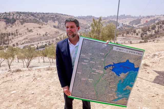 Israeli Finance Minister Bezalel Smotrich holds a map of an area near the settlement of Maale Adumim, a land corridor known as E1, outside Jerusalem in the occupied West Bank, on August 14, 2025, after a press conference at the site.