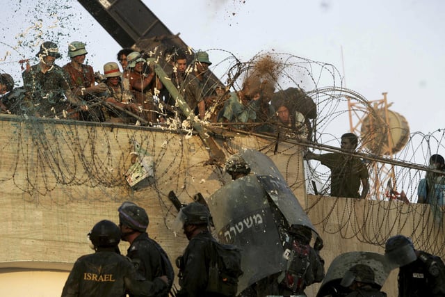 FILE - Israeli police officers storm the rooftop of a synagogue, battling dozens of protesters who threw acid, sand and buckets of green liquid and tried to hit officers with sticks, in the Jewish settlement of Kfar Darom, in the southern Gaza Strip, Aug. 18, 2005. (AP Photo/Lefteris Pitarakis)