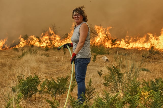 A woman with a hose tries to put out the fire during a wildfire in Santa Baia De Montes, northwestern Spain, Thursday, Aug. 14, 2025. (AP Photo/Lalo R. Villar)