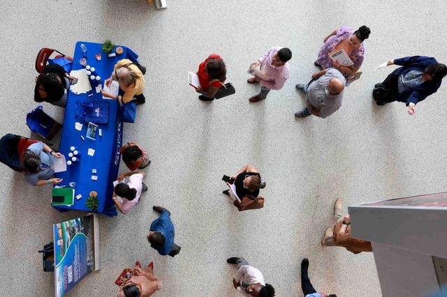 Job seekers wait in line to speak with recruiters at a job fair.