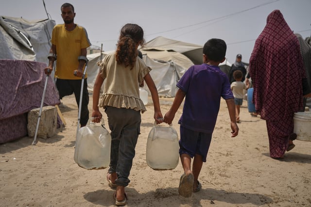 In the summer heat, Palestinian children carry jerrycans after collecting water from a distribution point in Gaza City, Tuesday, Aug. 12, 2025. (AP Photo/Jehad Alshrafi)