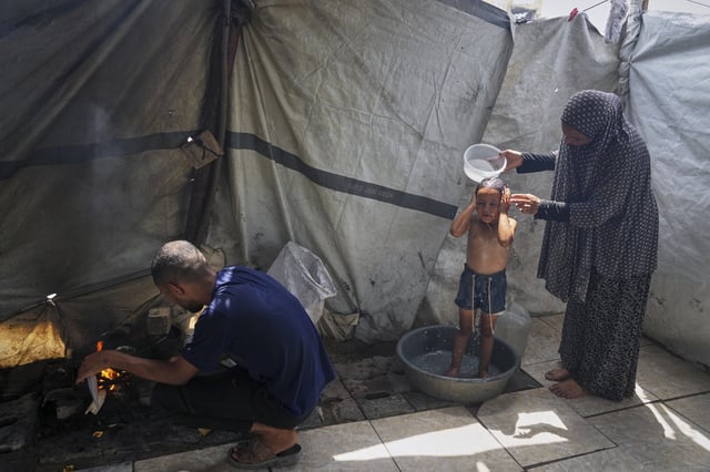 Enaam Al Majdoub uses water collected from a distribution point to bathe her 3-year-old granddaughter, Jourieh, while her son Zaki uses some of the water for cooking in their family tent in Gaza City on Tuesday, August 12, 2025. (AP Photo/Jehad Alshrafi)