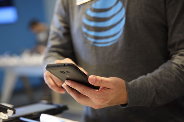 An employee assist a customer with a smartphone at an AT&T Inc. store in Newport Beach, California, on Thursday, Aug. 10, 2017.