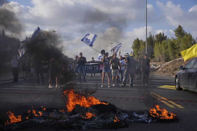 Demonstrators block a road during a protest demanding the immediate release of hostages held by Hamas and calling for the Israeli government to reverse its decision to take over Gaza City and other areas in the Gaza Strip, near Jerusalem, Israel, Sunday, Aug. 17, 2025. (AP Photo/Ohad Zwigenberg)