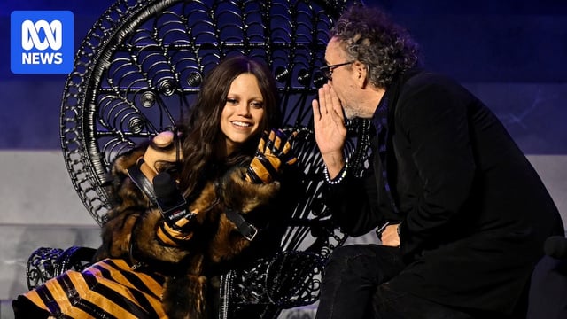 Tim Burton whispering in Jenna Ortega's ear on stage