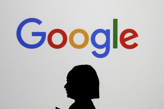 FILE - A woman walks by a giant screen with a logo at an event at the Paris Google Lab on the sidelines of the AI Action Summit in Paris, on Feb. 9, 2025. (AP Photo/Thibault Camus,File)