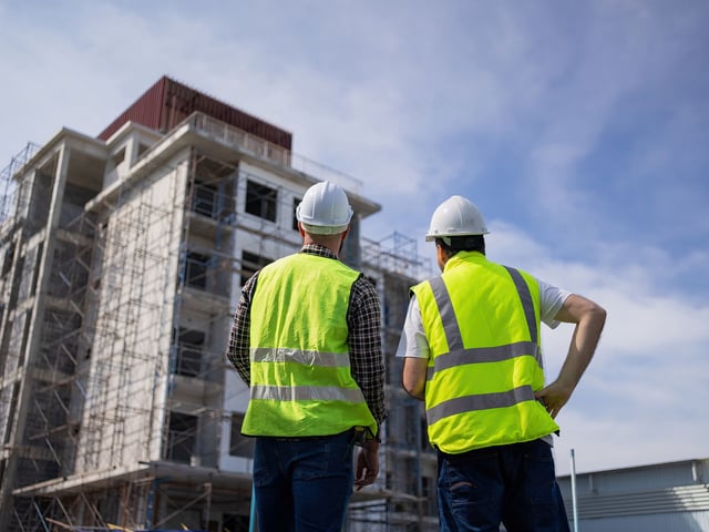 Engineers in hard hats inspect a large building covered in scaffolding. 