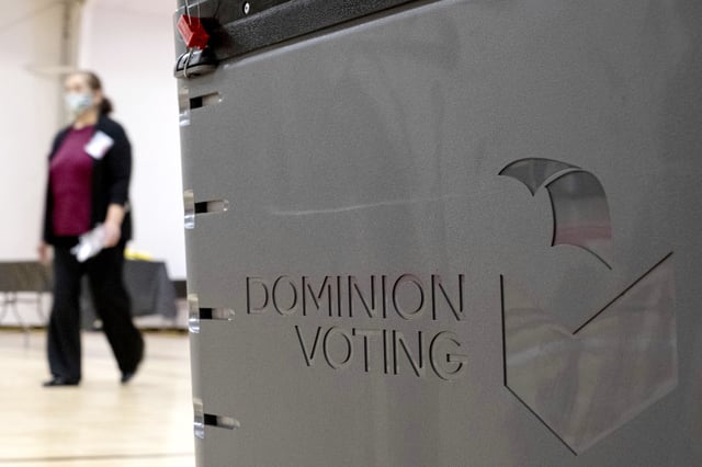 FILE - A worker passes a Dominion Voting ballot scanner while setting up a polling location at an elementary school in Gwinnett County, Ga., outside of Atlanta on Jan. 4, 2021. (AP Photo/Ben Gray, File)