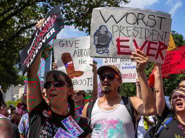 Jessica Bunting, left, and Jacob Serrano, right, hold up signs during the Fight the Trump Takeover rally at the Texas Capitol, Saturday, Aug. 16, 2025, in Austin, Texas. (Aaron E. Martinez/Austin American-Statesman via AP)