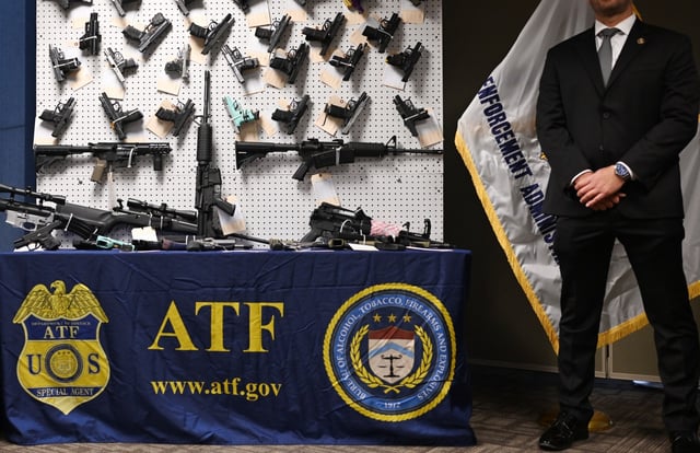 An agent stands next to a wall of seized firearms during a news conference at the Bureau of Alcohol, Tobacco, Firearms and Explosives offices in Denver on Aug. 18, 2025. (Photo by RJ Sangosti/The Denver Post)