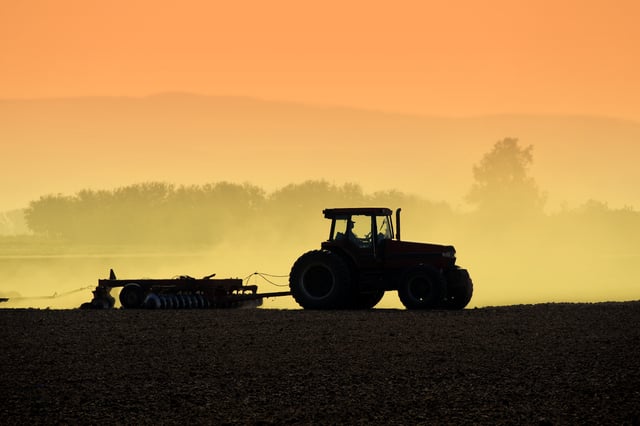 Muted backlit silhouette of two tractors raking soil in California’s San Joaquin Valley.