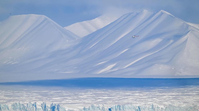 Ein Hubschrauber fliegt über einen Gletscher im Osten von Spitzbergen, im Svalbard-Archipel. 
