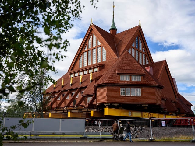 Menschen betrachten die Kiruna-Kirche, eine schwedisch-lutherische Holzkirche im samischen Stil, die auf Schwedisch Kiruna Kyrka heißt, einen Tag bevor sie im Rahmen der Umsiedlung der Stadt auf einer 5 Kilometer langen Strecke nach Osten in ein neues Stadtzentrum verlegt wird.