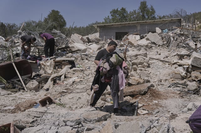 A Palestinian youth carries clothes as he walks over the rubble of a house demolished by the Israeli army in the West Bank village of Beit Sira, near Ramallah, Tuesday, Aug. 19, 2025. (AP Photo/Mahmoud Illean)