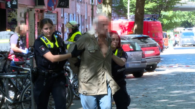 Zwei Beamtinnen der Polizei führen den Mann in Gewahrsam ab.