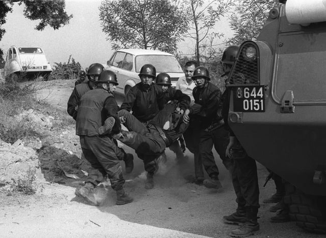 Des gendarmes évacuent un collègue blessé lors de leur intervention pour libérer six hommes pris en otage par des indépendantistes corses masqués et armés dans la cave à vin « Sovicor » à Aléria, en Corse, le 22 août 1975